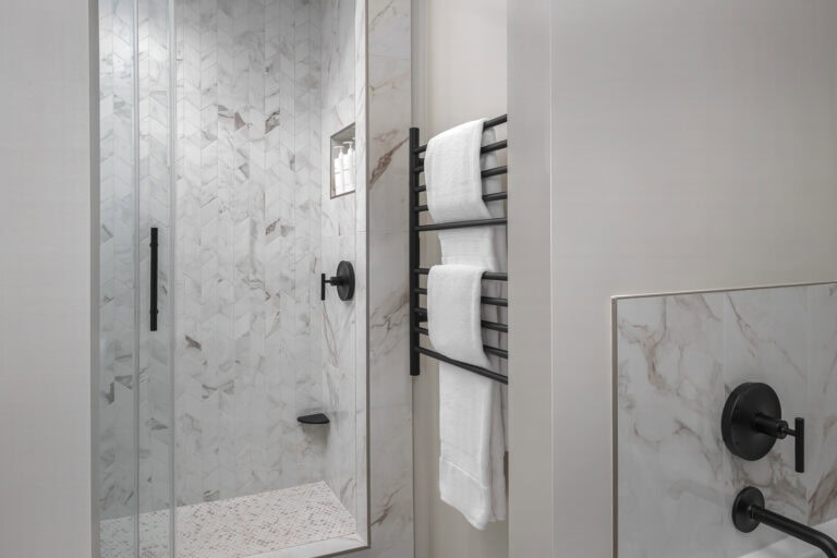 The Merchant Suite bathroom features marble-look tiles, a walk-in glass shower, and a heated towel rack. Clean lines and modern fixtures create a calming, rejuvenating experience.