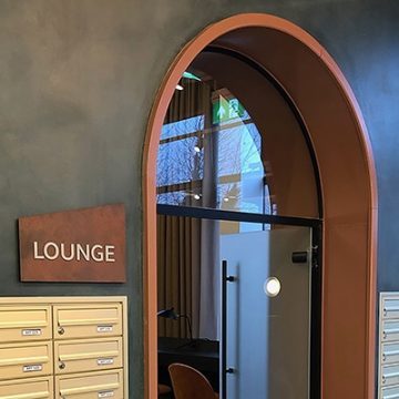 Photograph of a sign for the lounge in Brook Place Apartments made from a corten laminate, reflecting the materials used on the exterior of the building.