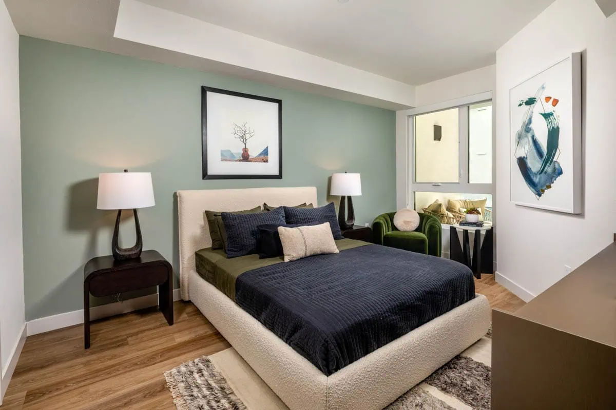 A bedroom with a bed and two side tables with lamps, and a window at The Wyatt apartments in San Diego.