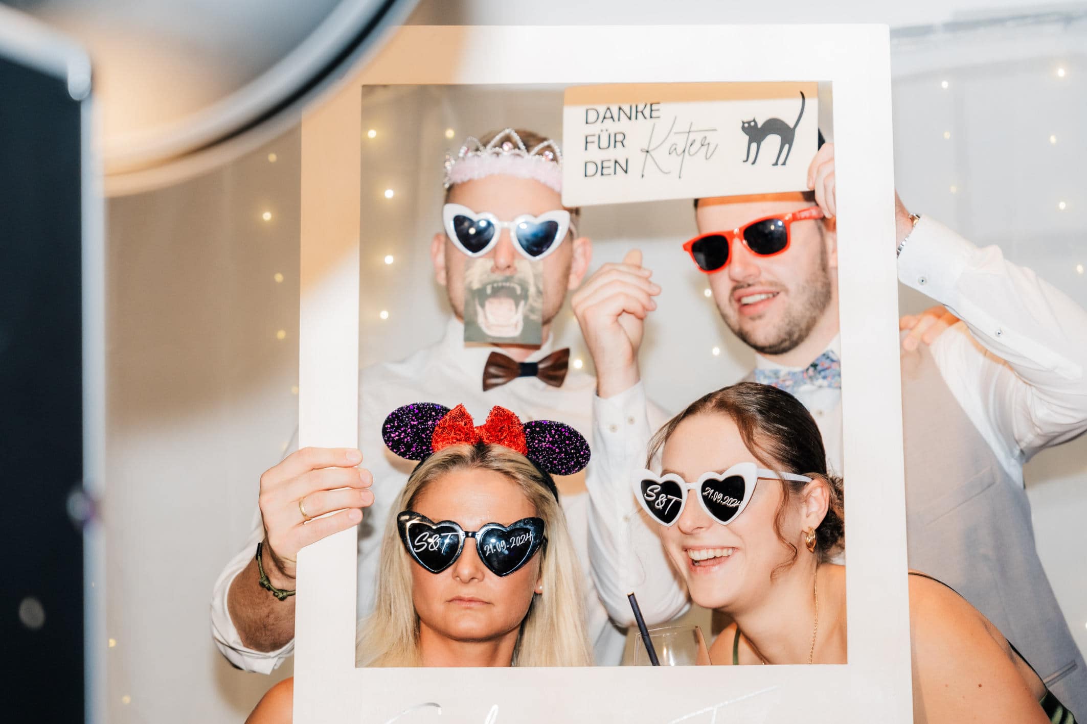 vier Freunde die eine Fotobox zum vermieten bedienen und dabei Sonnenbrillen aufhaben 