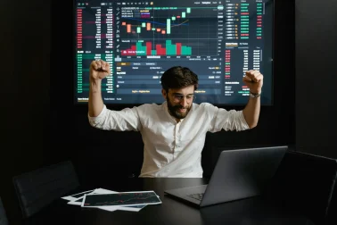 pexels-photo-7567565-7567565 Businessman celebrates stock market success with hands raised in excitement at a trading desk.