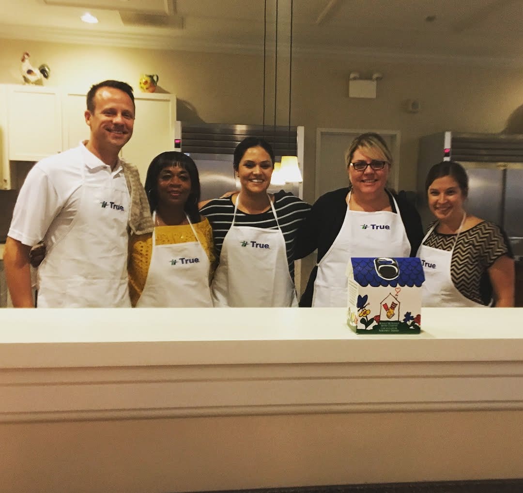 Group of people wearing aprons in a kitchen.