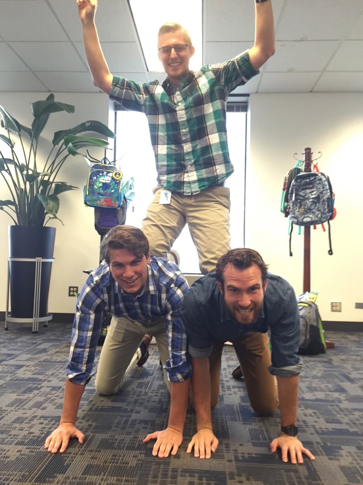 Three friends forming a human pyramid indoors.