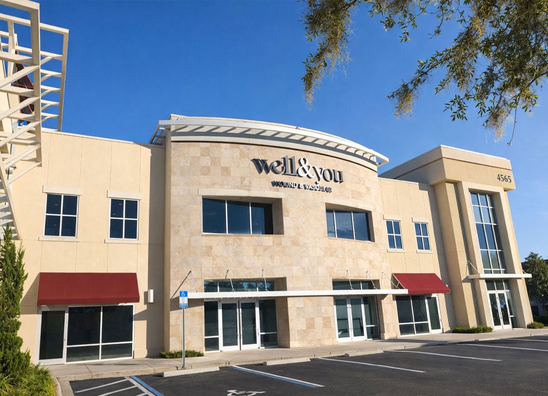 A modern clinic building with the sign "well & you WOUND & VASCULAR" above the entrance and two sets of large windows on the upper and lower levels.
