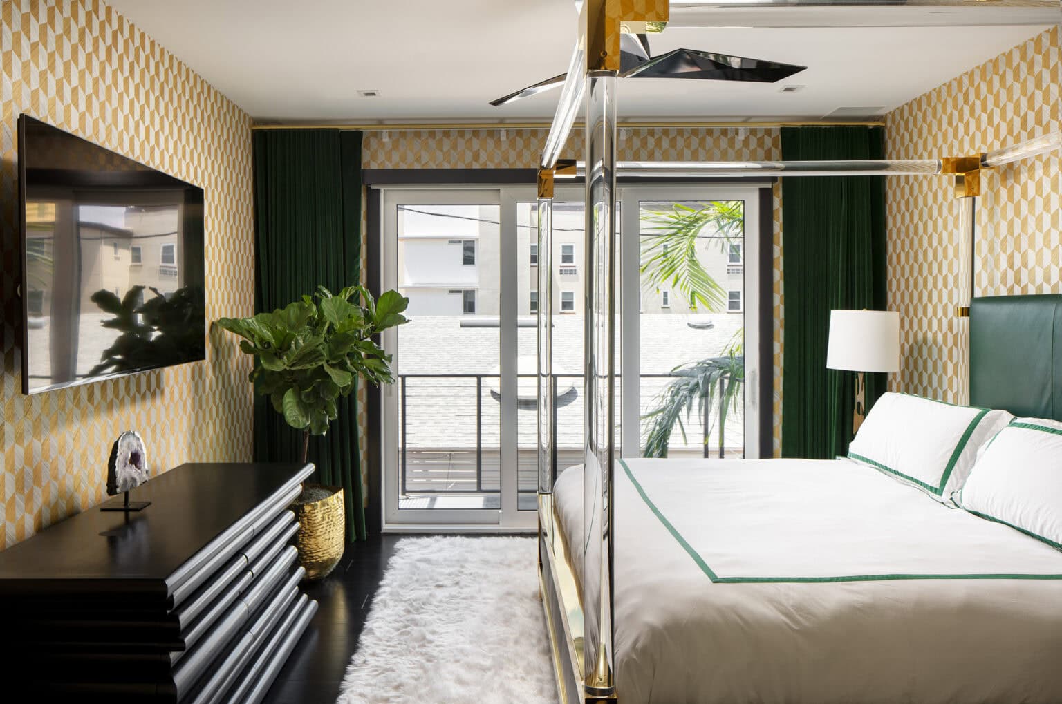 Bedroom with gold geometric wallpaper, a brass canopy bed with green-trimmed linens and deep green drapes