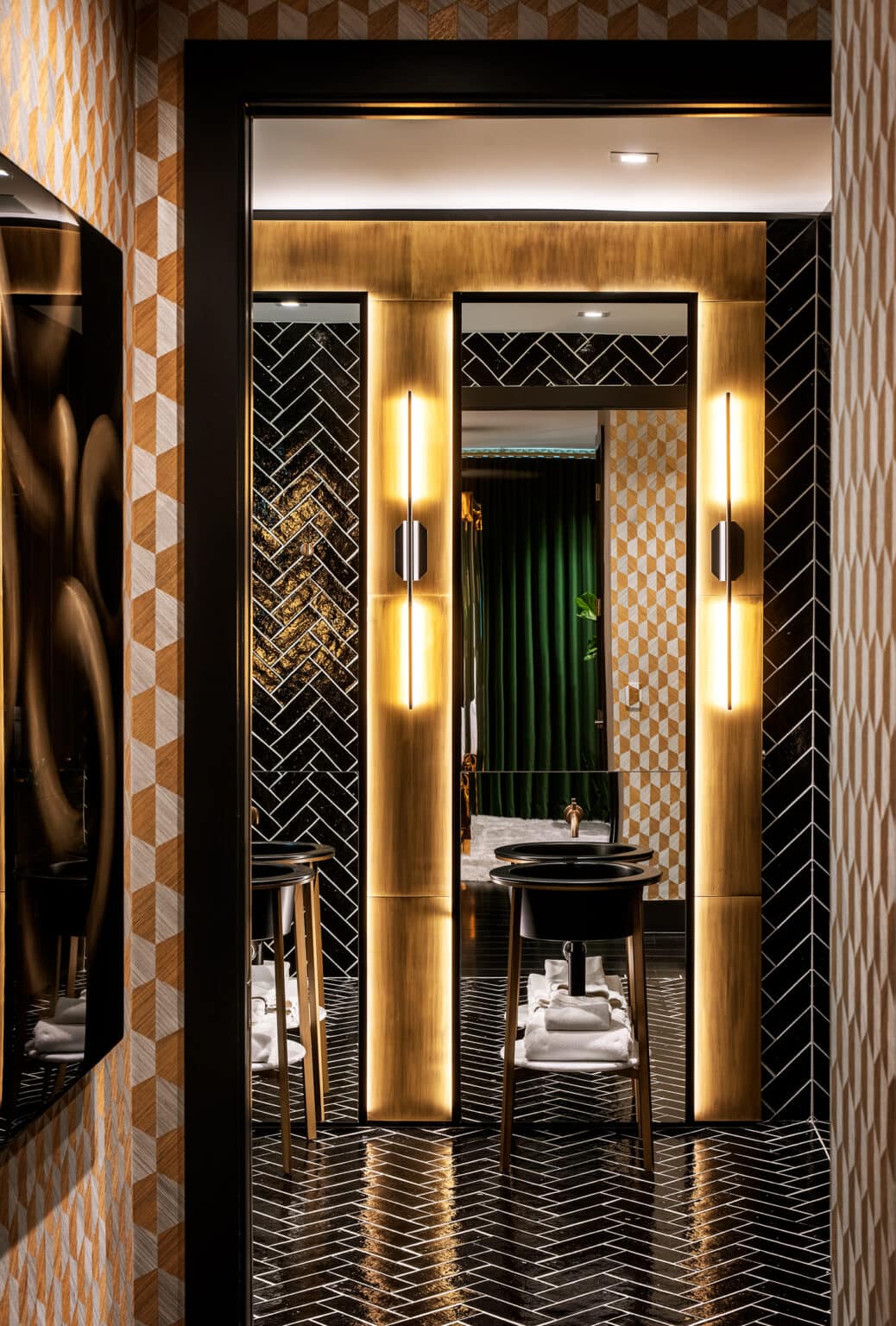 Bathroom entry with herringbone floor tile, backlit brass wall panels and a dark vanity beyond