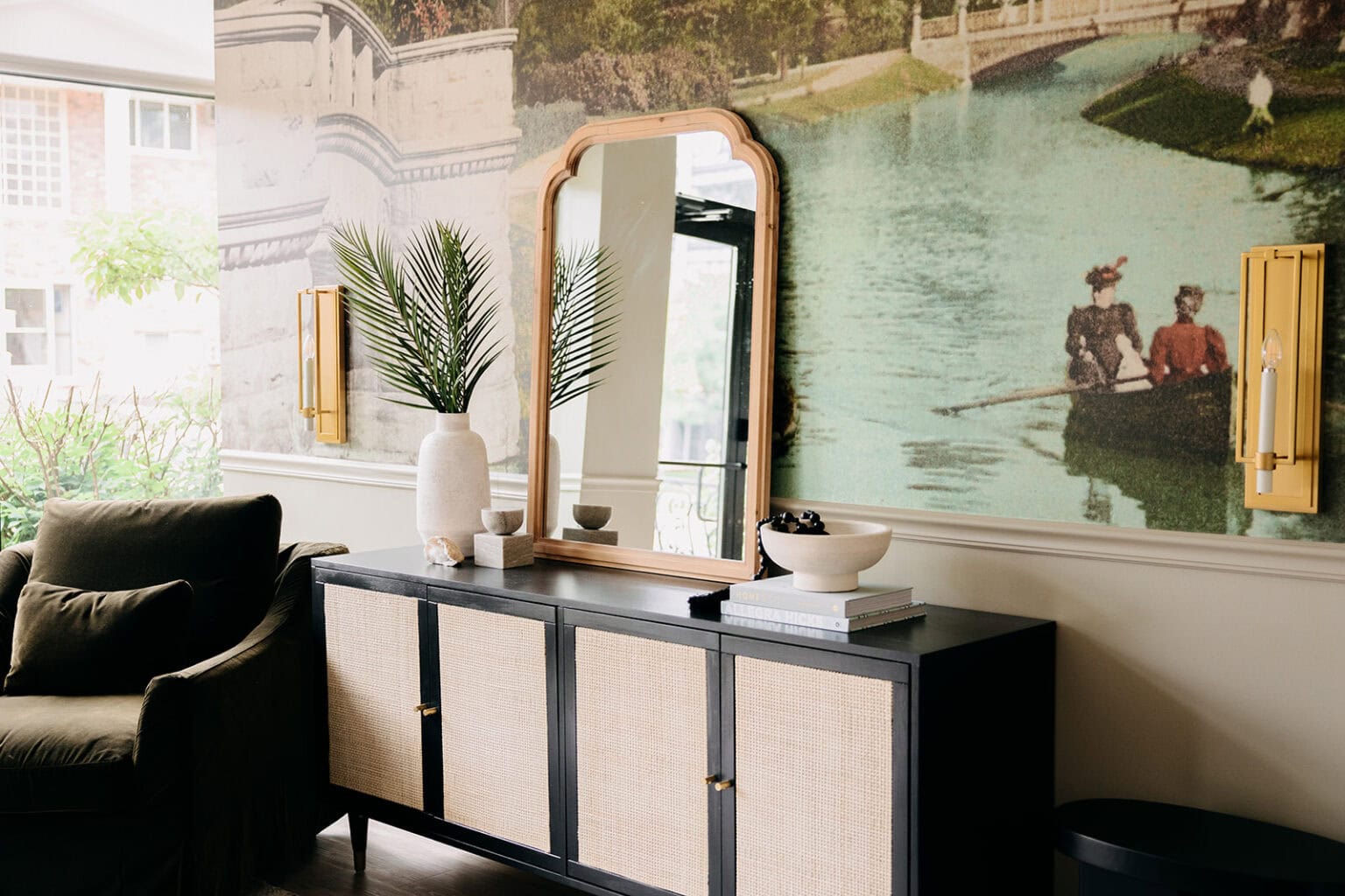 Sitting room with a hand-painted canal mural, an arched brass mirror, a cane-front cabinet and a dark velvet armchair