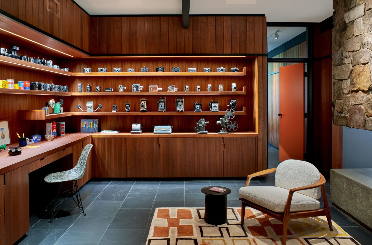 Walnut-paneled study with built-in shelving, a desk, a cream lounge chair and a patterned rug