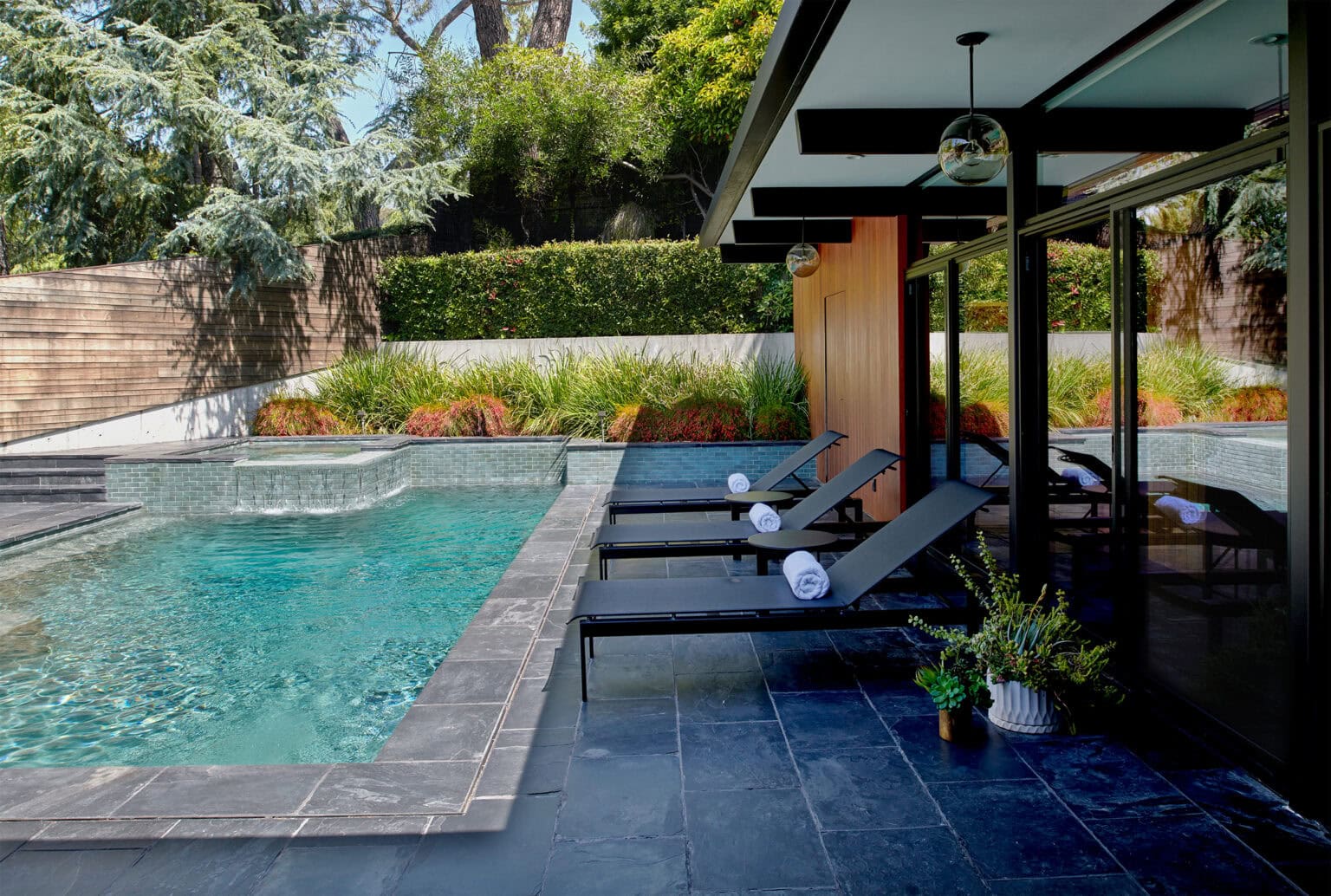 Backyard pool with a stone deck, black lounge chairs and a covered modern patio