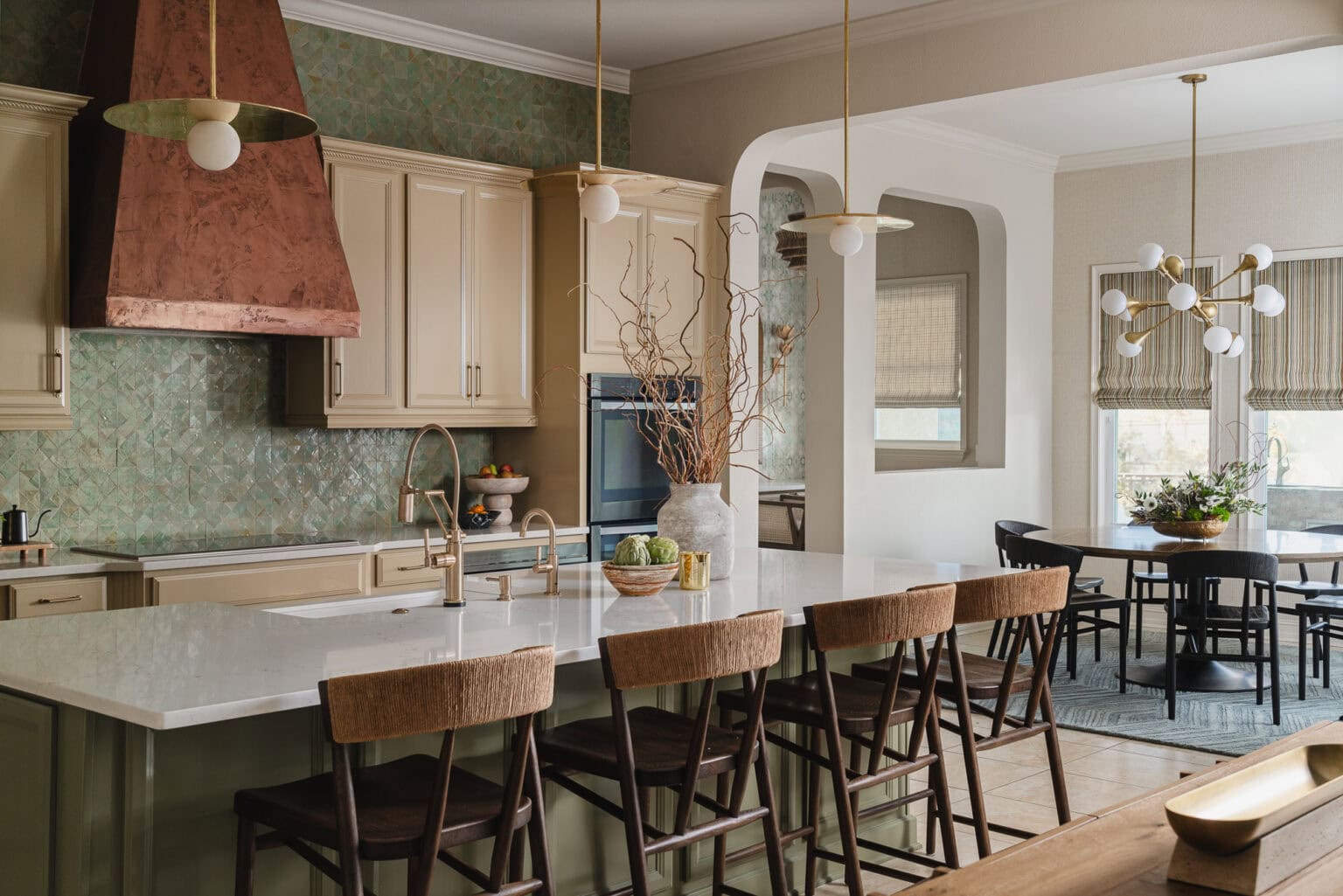 Open kitchen and dining room with a copper hood, marble island and wood counter stools, with a dining table beyond