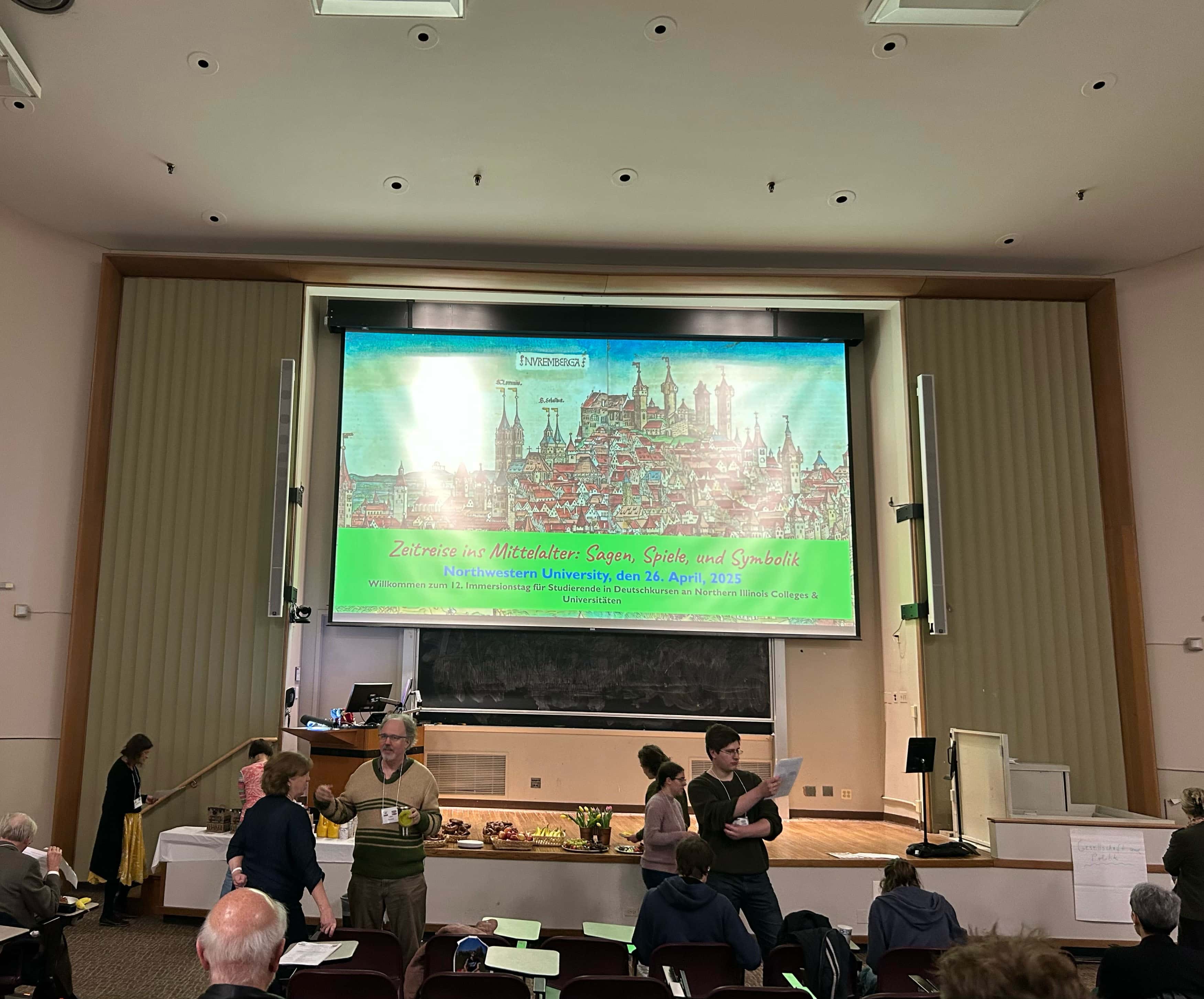 Screen with green graphic. people gathering and talking to each other in an auditorium.