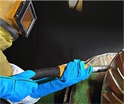 Imagel depicts a man in protective gear, engaged in the process of sandblasting