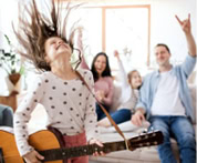 Image of a 12-year-old girl energetically strumming her guitar takes center stage, while in the background, her family shares hearty laughter while gathered on a sofa.