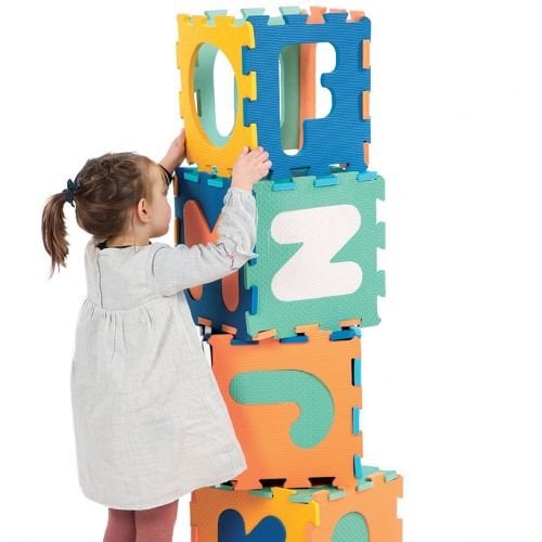 Une petite fille se tient à côté d’une pile de Ludi - Tapis Dalles Lettres.