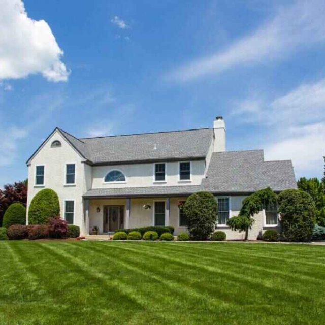 White home with gray roof with large lawn and blue sky