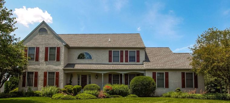 sandstone home with new roof with surrounding lawn and shrubs