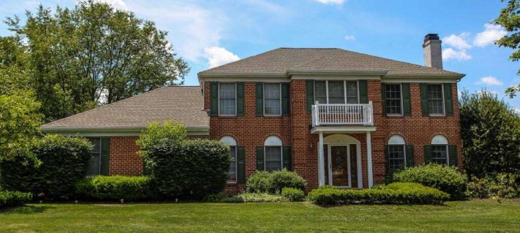 two story red brick home with new roof with lawn and trees