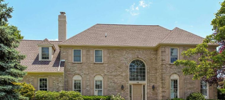 white brick home with new roof surrounded by lawn and shrubs