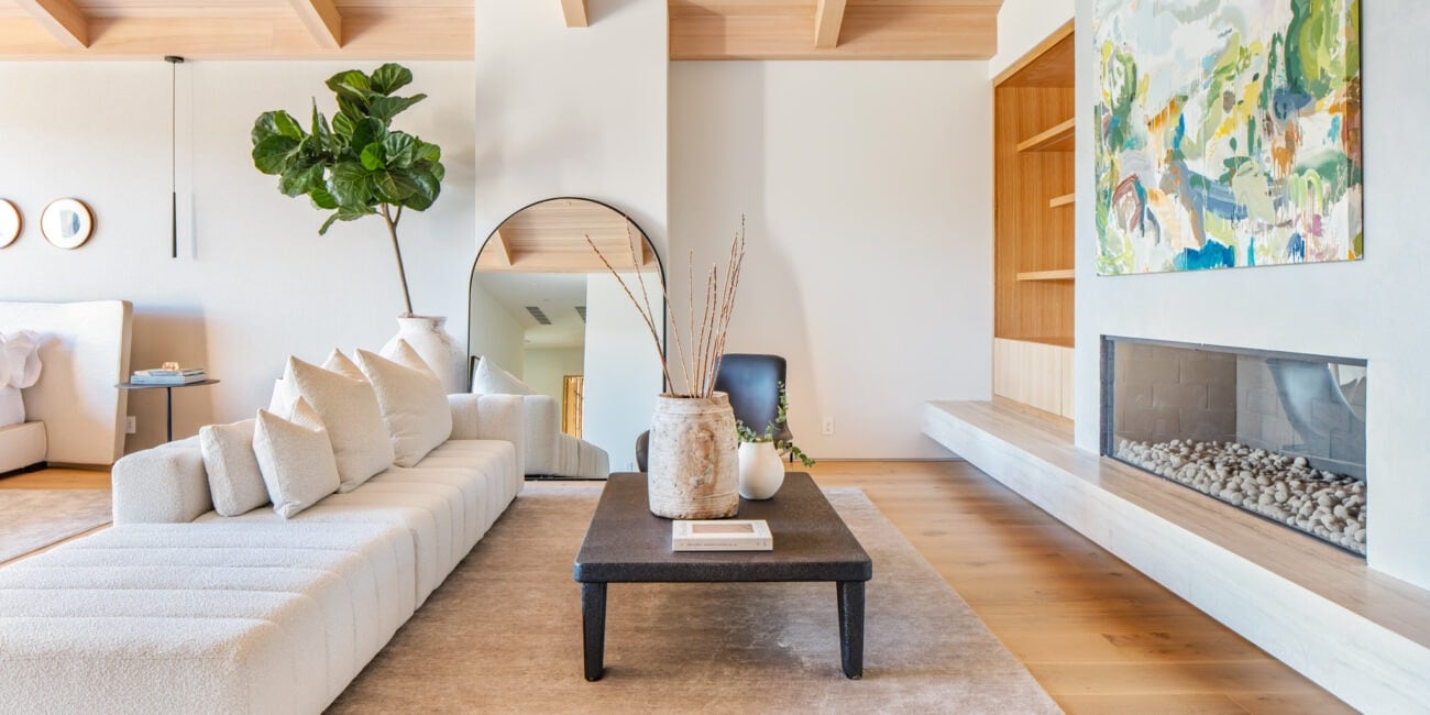 Fuzzy, modern living room with minimalist white sofa, natural wood ceiling beams, and a sleek built-in fireplace.