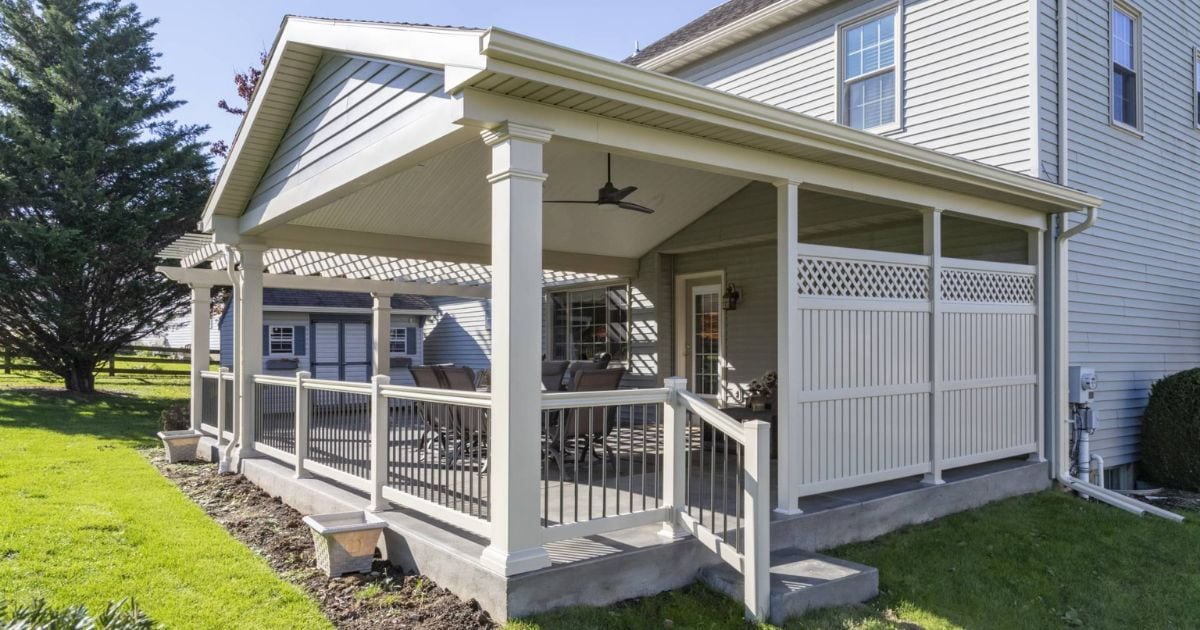attached covered porch addition with concrete foundation and white vinyl railing around the outside of it and outdoor furniture seated on it