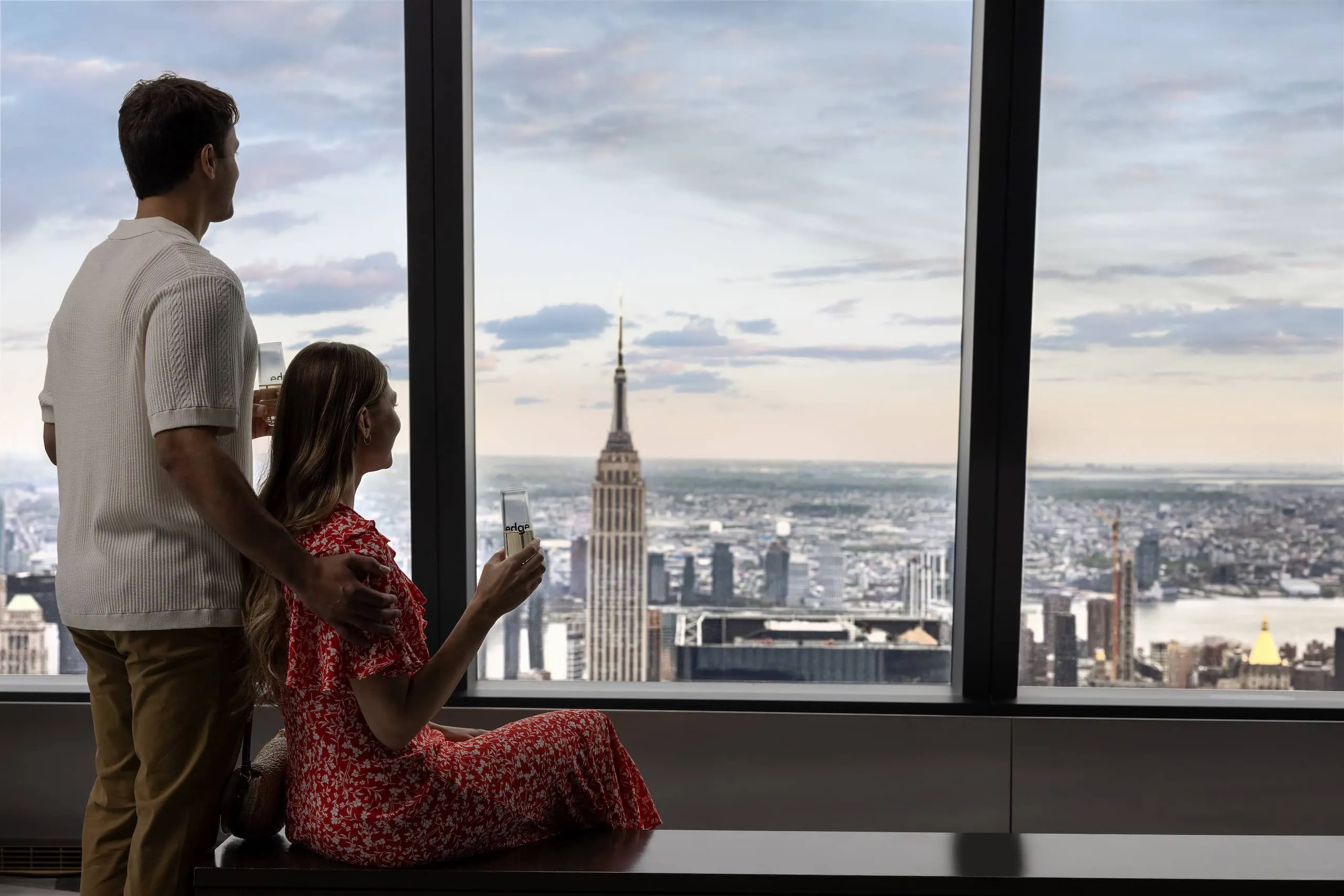A couple look at the view of New York City form the indoor seating area at The Edge while enjoying champagne