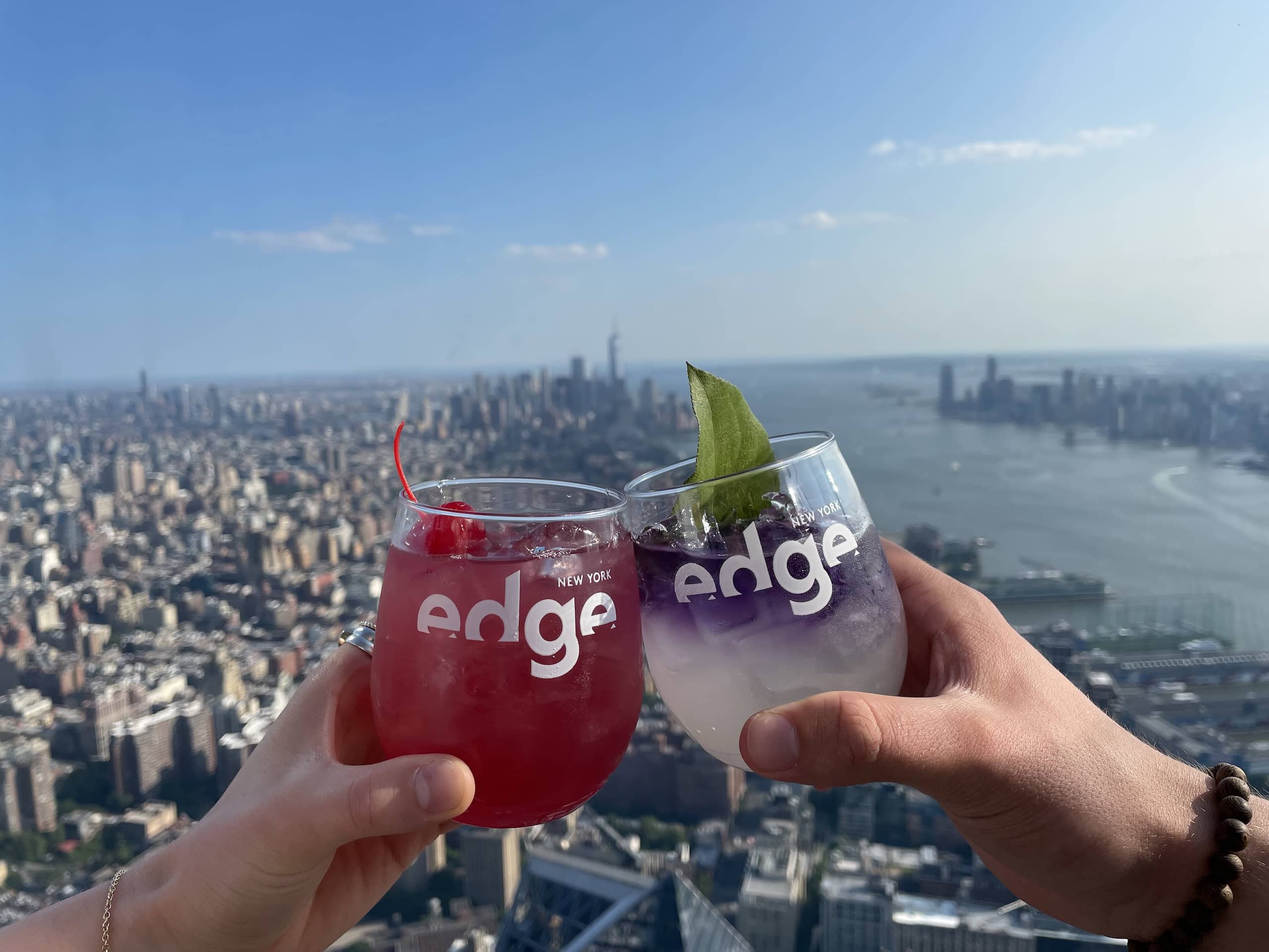 Two people clink glasses with cocktails overlooking New York city on a sunny day