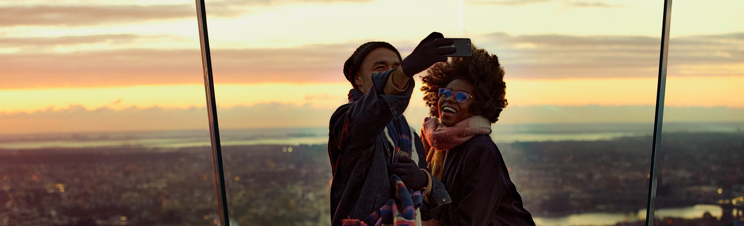 A couple posing for a selfie at the eastern point of The Edge NYC during sunset