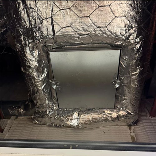 A fire damper inspection hatch in a heavily padded rectangular ventilation pipe.