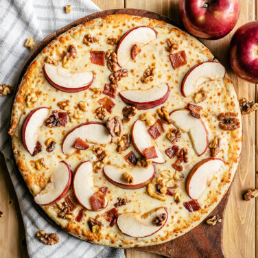 Pizza topped with apple slices, bacon, and walnuts