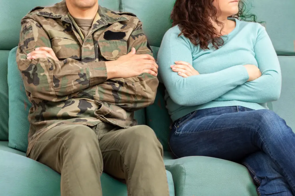 Military Benefits in Divorce | A military service member with his wife sitting on a couch with arms crossed.