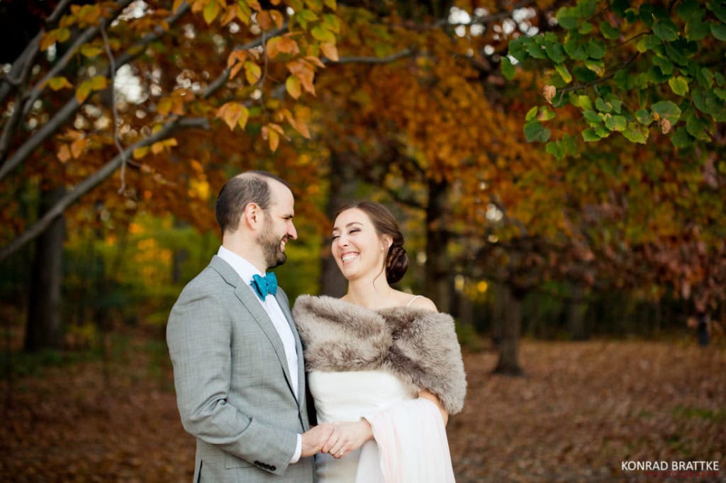 A bride and groom smiling in Prospect Park during their fall leaves wedding.