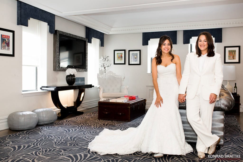 A bride in a white dress standing next to a bride in a white suit, elegantly exchanging vows at their Manhattan Penthouse wedding.