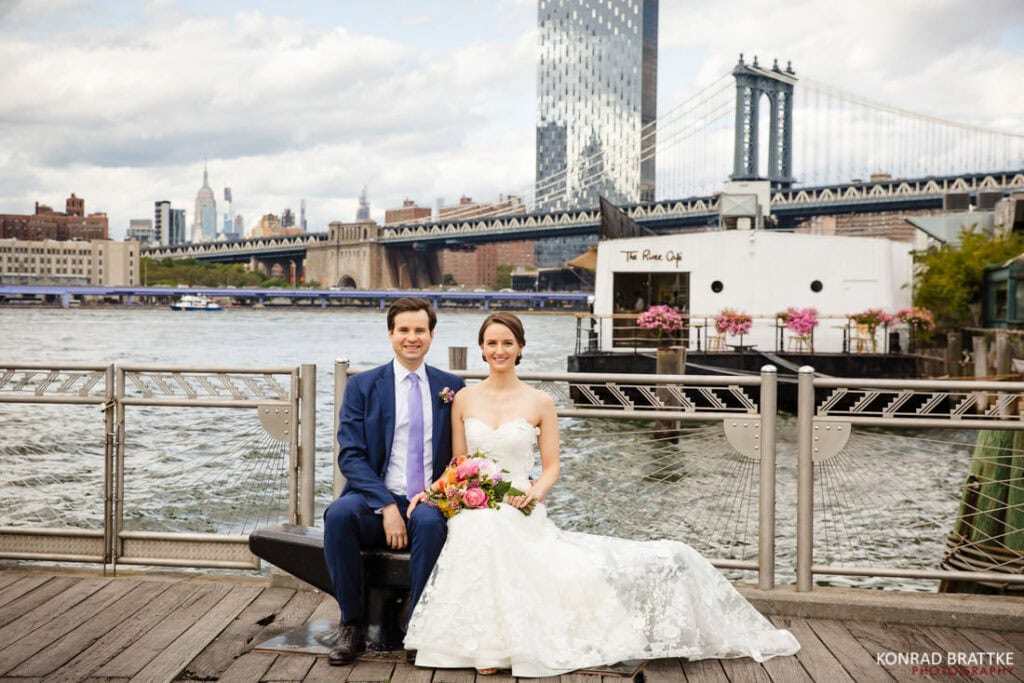 A bride and groom posing on a dock in front of the river cafe in Brooklyn, NY.
