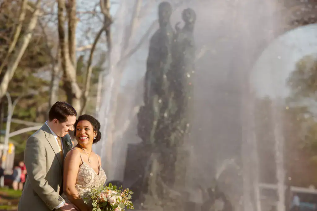 A bride and groom standing in front of a fountain in Brooklyn, New York.