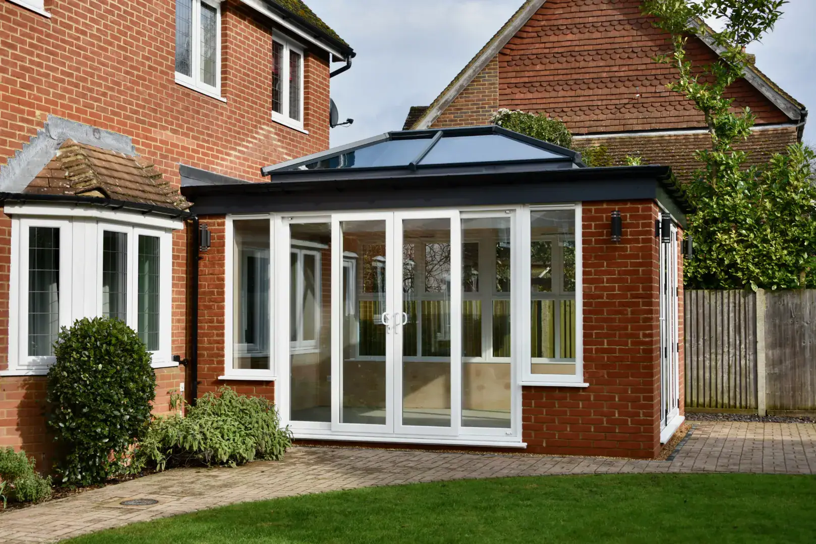 Brick orangery extension with white framed sliding doors, black roofline and a lawn garden outside.