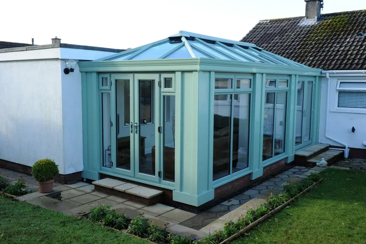 Pale green orangery kitchen extension with a glazed roof, French doors and garden patio access.