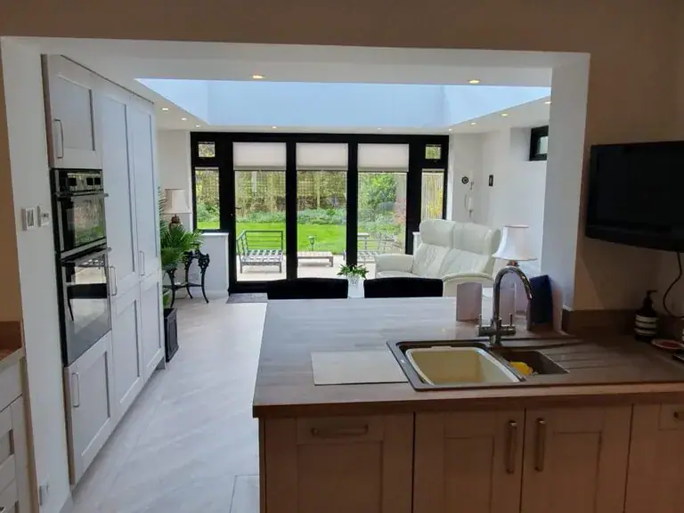 Open kitchen and lounge extension with black framed garden doors, white sofa and sink in the foreground.