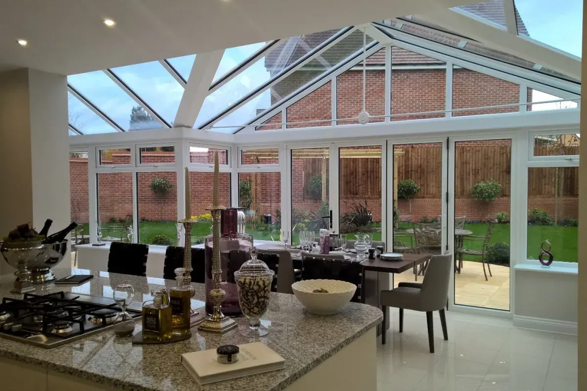 Open-plan kitchen extension with white conservatory glazing, garden doors, dining area and glass roof.