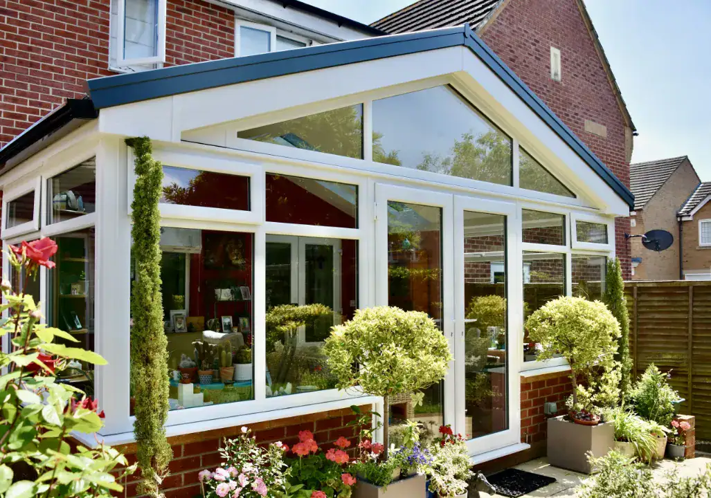 White gable end conservatory with large glazed panels, brick dwarf wall and landscaped planters outside.