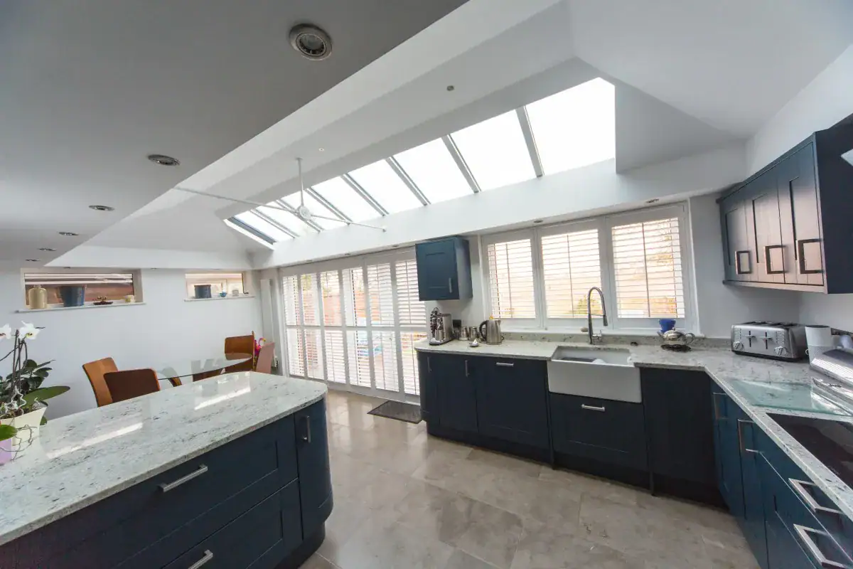 Kitchen extension with navy cabinets, marble worktops, rooflights, white shutters and glazed garden doors.