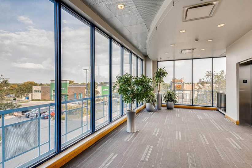 Modern office hallway with large windows and potted plants, part of Office Evolution coworking space.