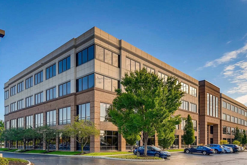 Modern office building exterior with large windows and parking lot, offering flexible coworking and workspace solutions.