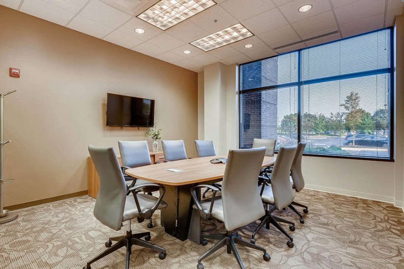 Modern office conference room with large window, ergonomic chairs, and flat-screen TV, ideal for meetings and collaborative work.