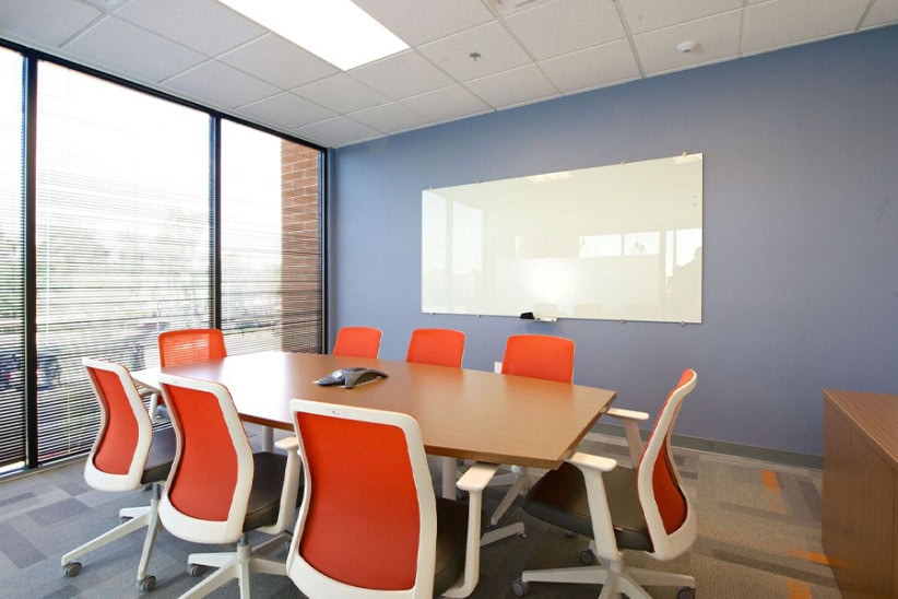 Modern office conference room with large window, orange ergonomic chairs, and whiteboard for business meetings and collaborative work.