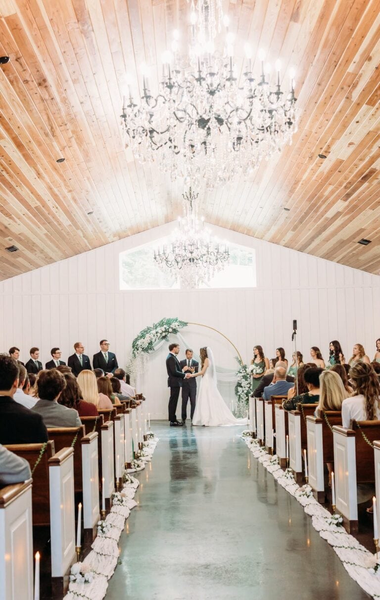 Erina and Nick exchange vows under a gold floral arch in the Romaine Valley chapel beneath crystal chandeliers