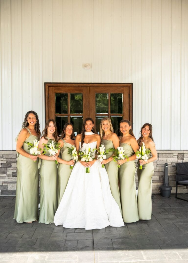 Bride Grace with her bridesmaids in sage green dresses holding white calla lily bouquets at Romaine Valley Weddings & Events in Fenton, MO
