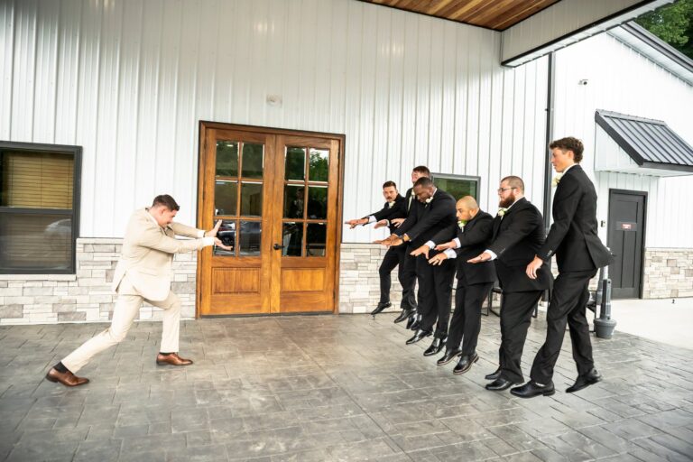 Groom Noe playfully posing with his groomsmen on the covered patio at Romaine Valley Weddings & Events in Fenton, MO