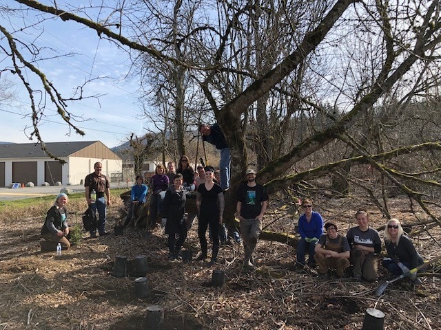 A planting day crew gathered for a group photo under a large mature tree in a cleared area along Tibbetts Creek