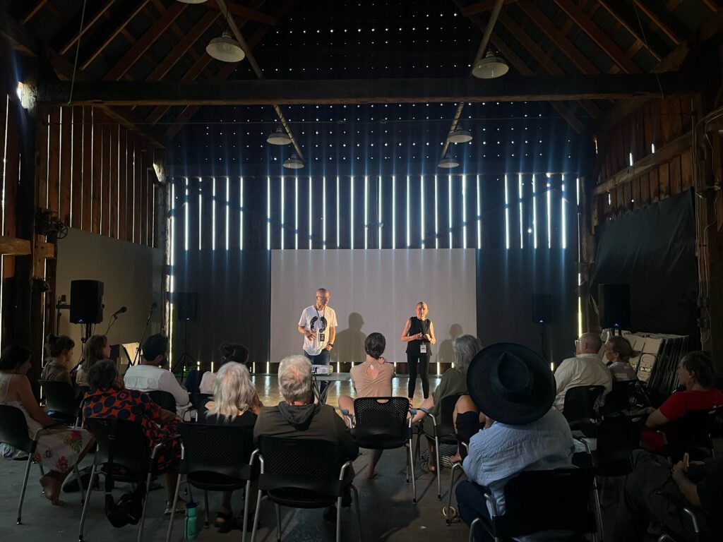 Barbara Bourget and Jay Hirabayashi lead a butoh workshop inside the barn at the Jeffrey Rubinoff Sculpture Park, standing in front of an audience.