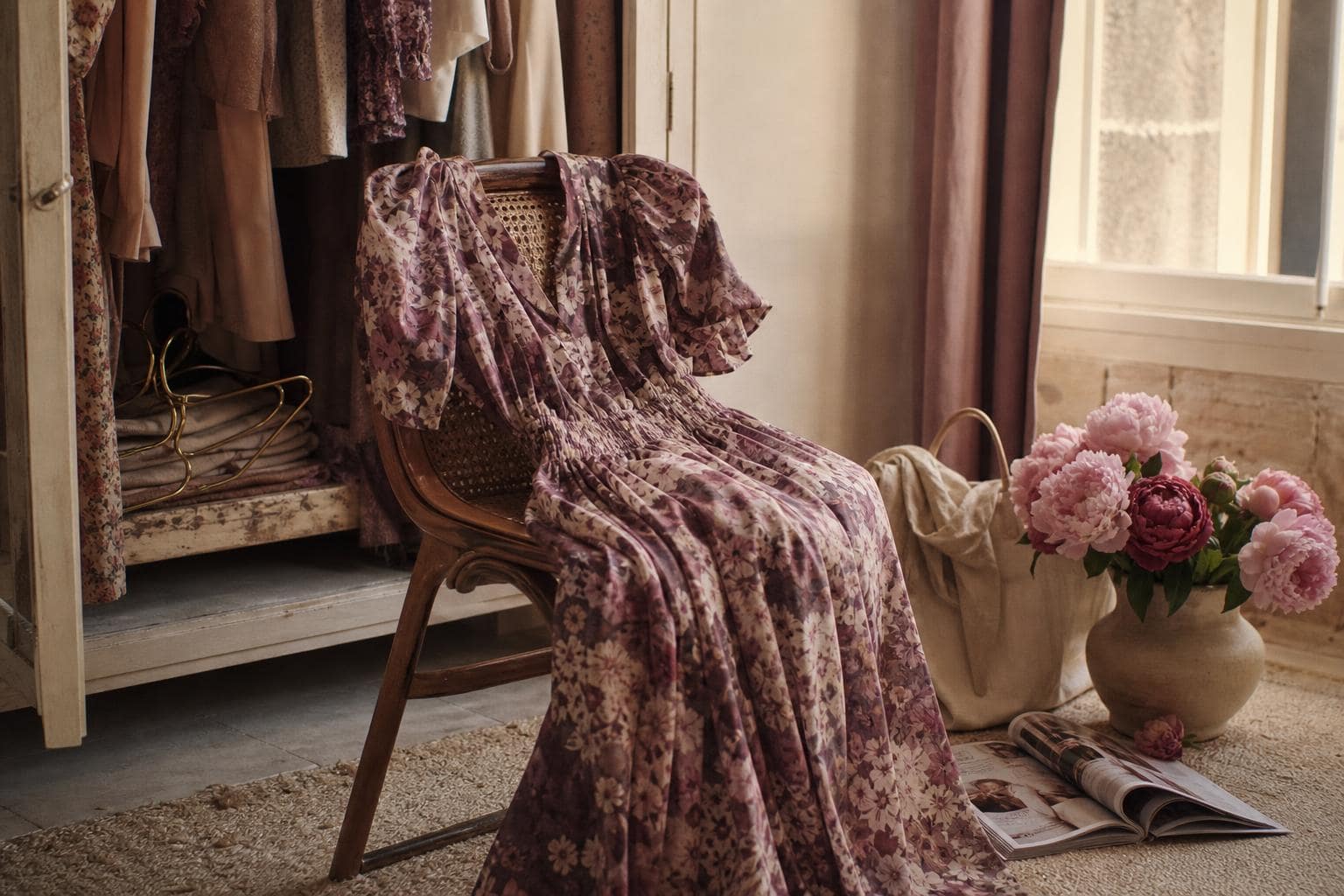 Robe en soie imprimée Ganni dans des tons prune et rose poudré, drapée sur une chaise en rotin près d'un placard ouvert